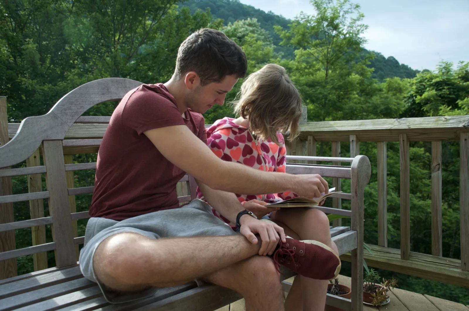 Daniel reading with a child on a porch at a summer camp
